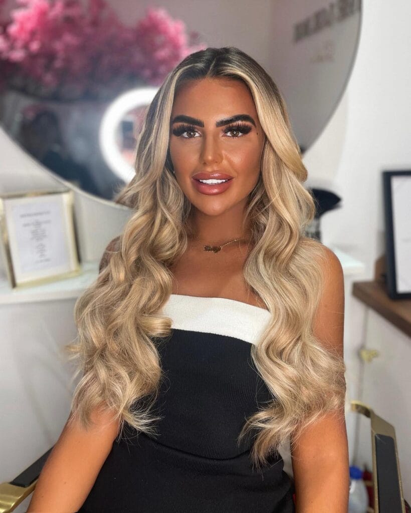 A woman with very long ash blonde hair styled in voluminous structured waves with a center part.