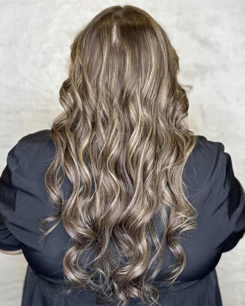 Long blonde hair styled in defined waves with soft blended highlights.