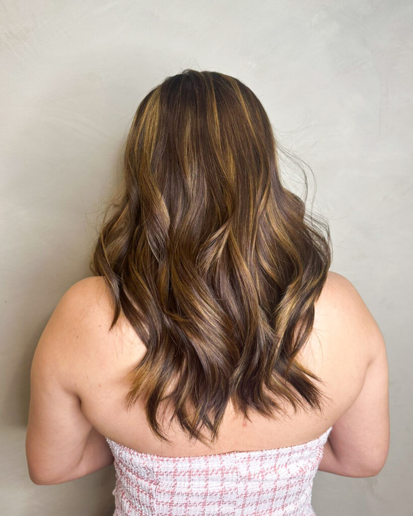 Long brunette layered hair with soft waves and subtle highlights.