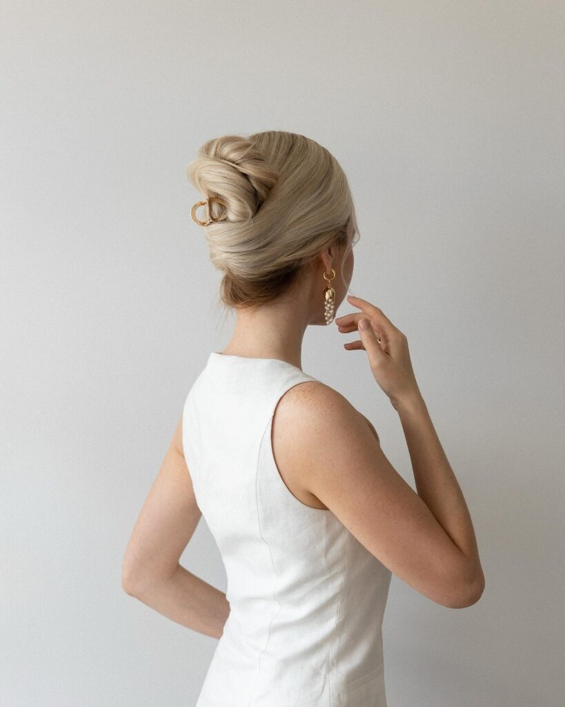 A woman with ash blonde hair from behind shows a sleek and polished French twist secured with a small gold claw clip.