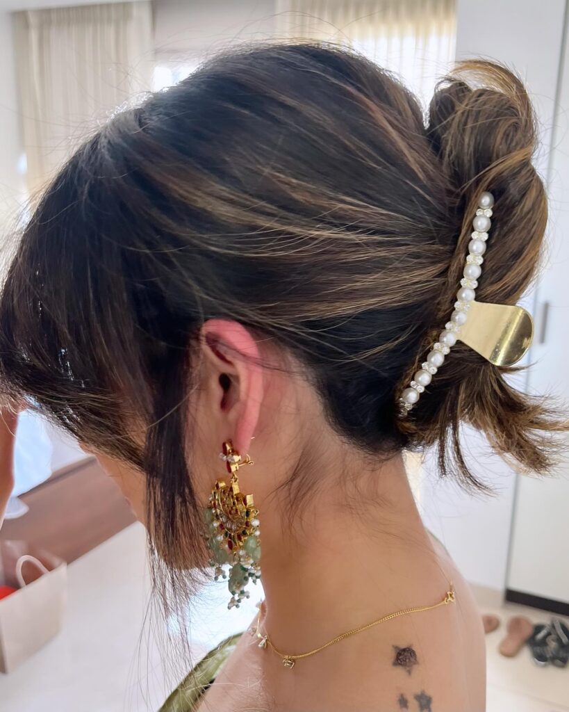 A woman with highlighted brown hair wears a textured French twist secured by a gold claw clip decorated with a row of white pearls.