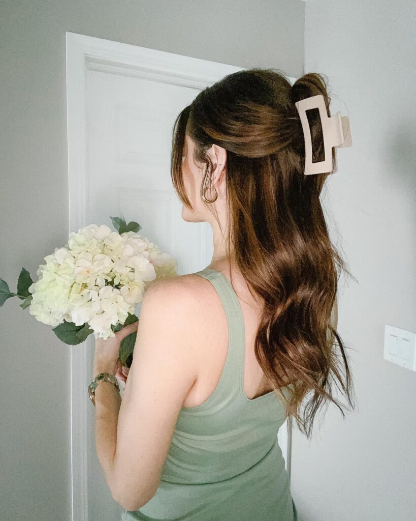 A woman with long wavy brunette hair wears a half up style secured with a large matte beige rectangular claw clip.