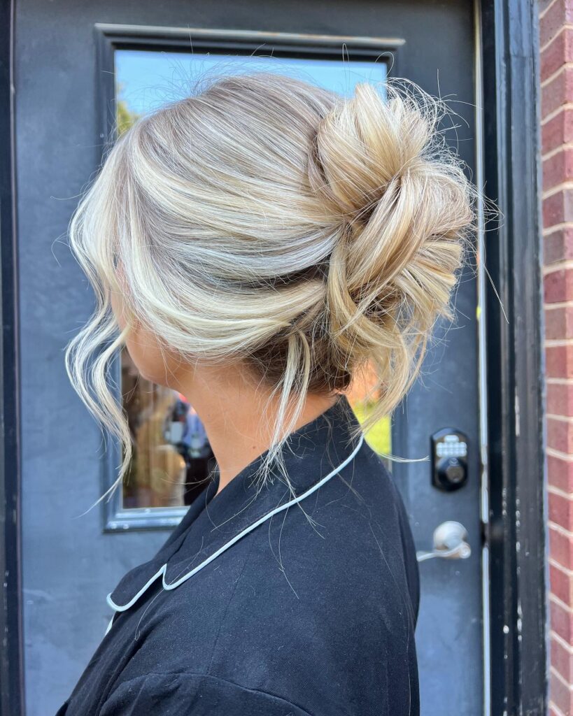 A woman with platinum blonde hair from behind shows a messy high bun secured by a modern claw clip with loose tendrils framing her face.