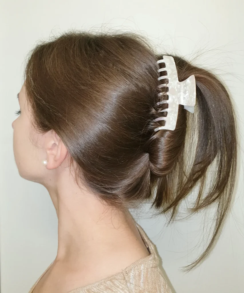 A woman with glossy brown hair wears a high ponytail twist secured by a large pearlescent white claw clip.