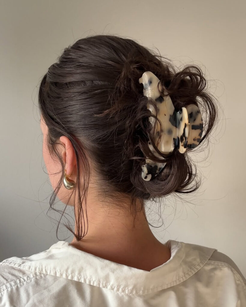 A woman with curly dark brown hair from behind wears an artfully messy low bun secured by a large tortoise shell patterned claw clip.