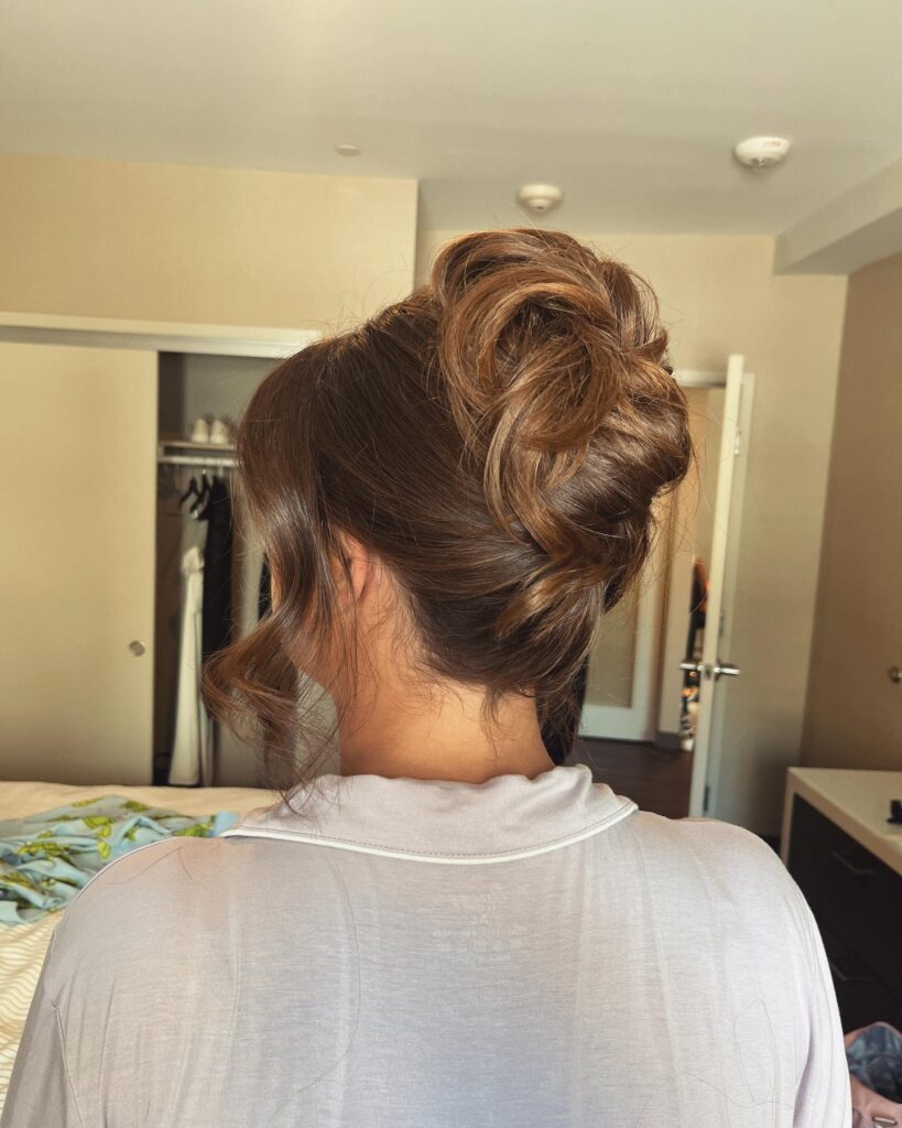 A woman from behind shows her medium brown hair styled into an intricate, swirled high bun with curled face framing tendrils.