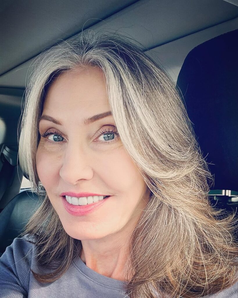 A woman with shoulder length layered hair, curtain bangs, and soft blonde highlights creating natural volume and movement.