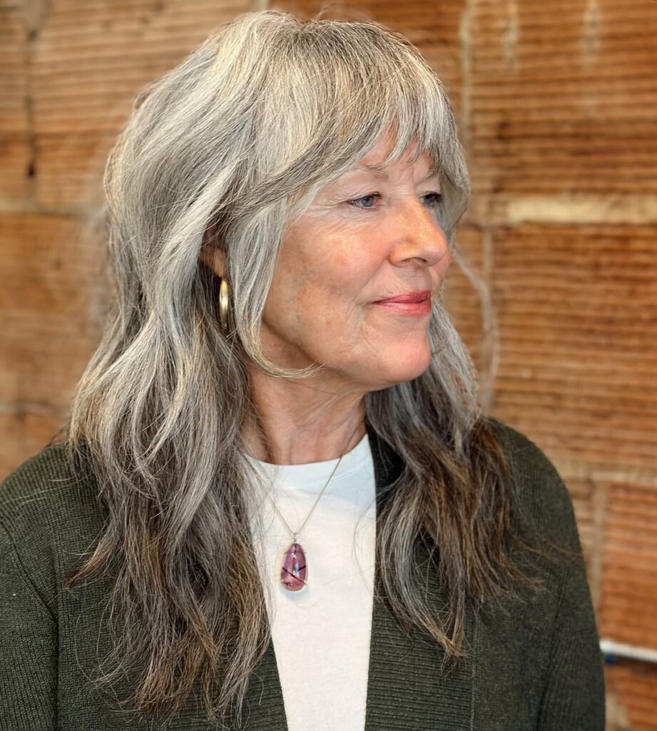 A woman with a long layered gray shag haircut and curtain fringe.