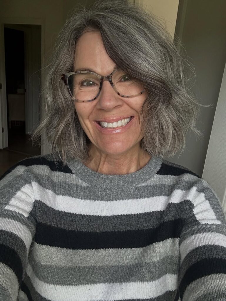 A woman with shoulder length layered salt and pepper hair and soft side swept bangs.