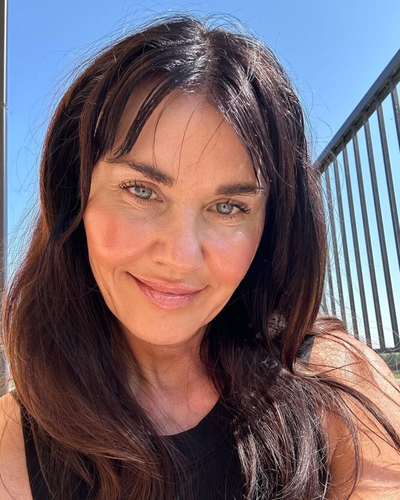 A woman with long layered dark hair and soft curtain bangs framing the face.
