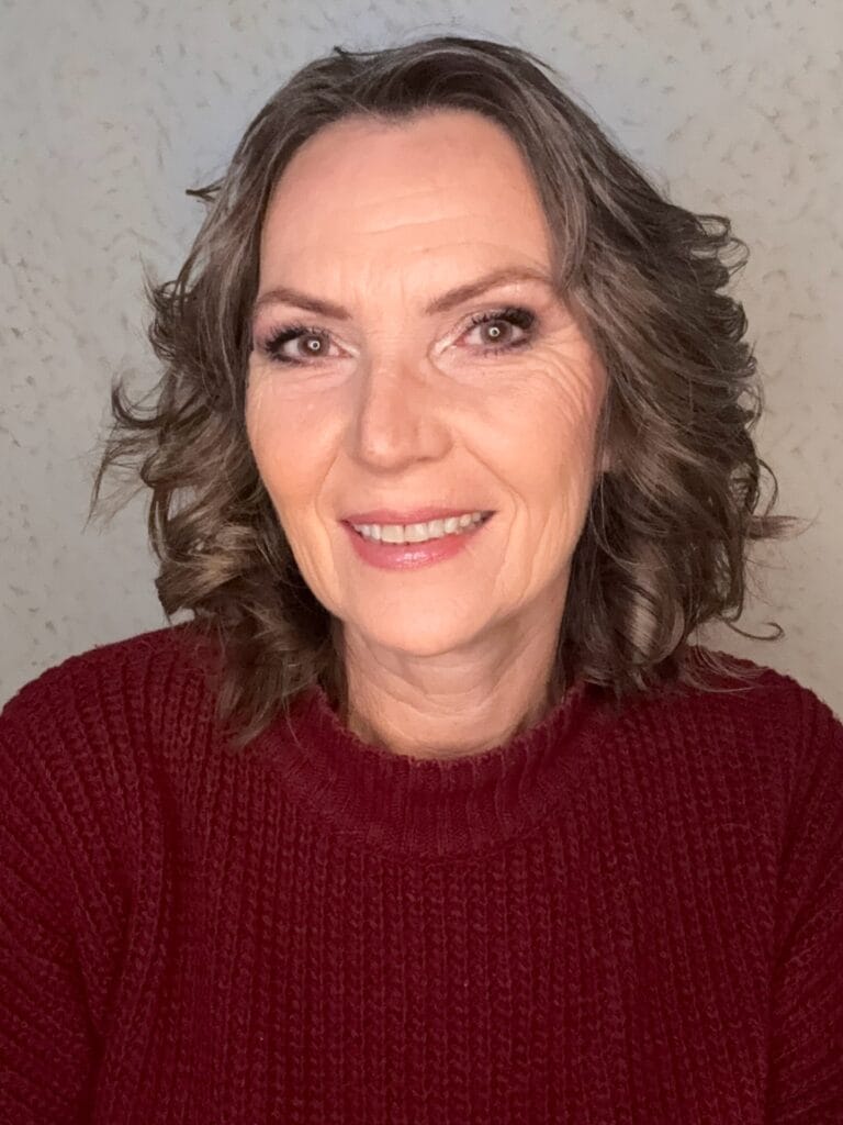 A woman with shoulder-length ash brown hair styled in soft, voluminous curls wearing a maroon sweater.