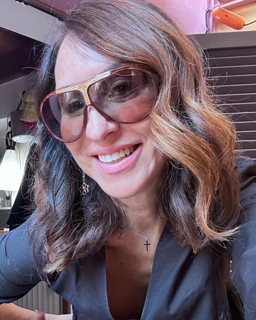 A woman with shoulder-length wavy brunette hair featuring warm caramel highlights and side-swept bangs.