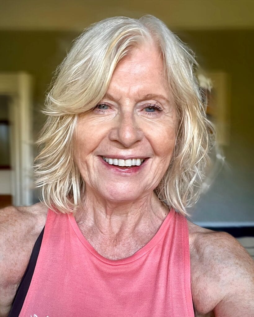 A smiling woman with shoulder-length bright champagne-blonde hair styled with flicked layers and soft waves.