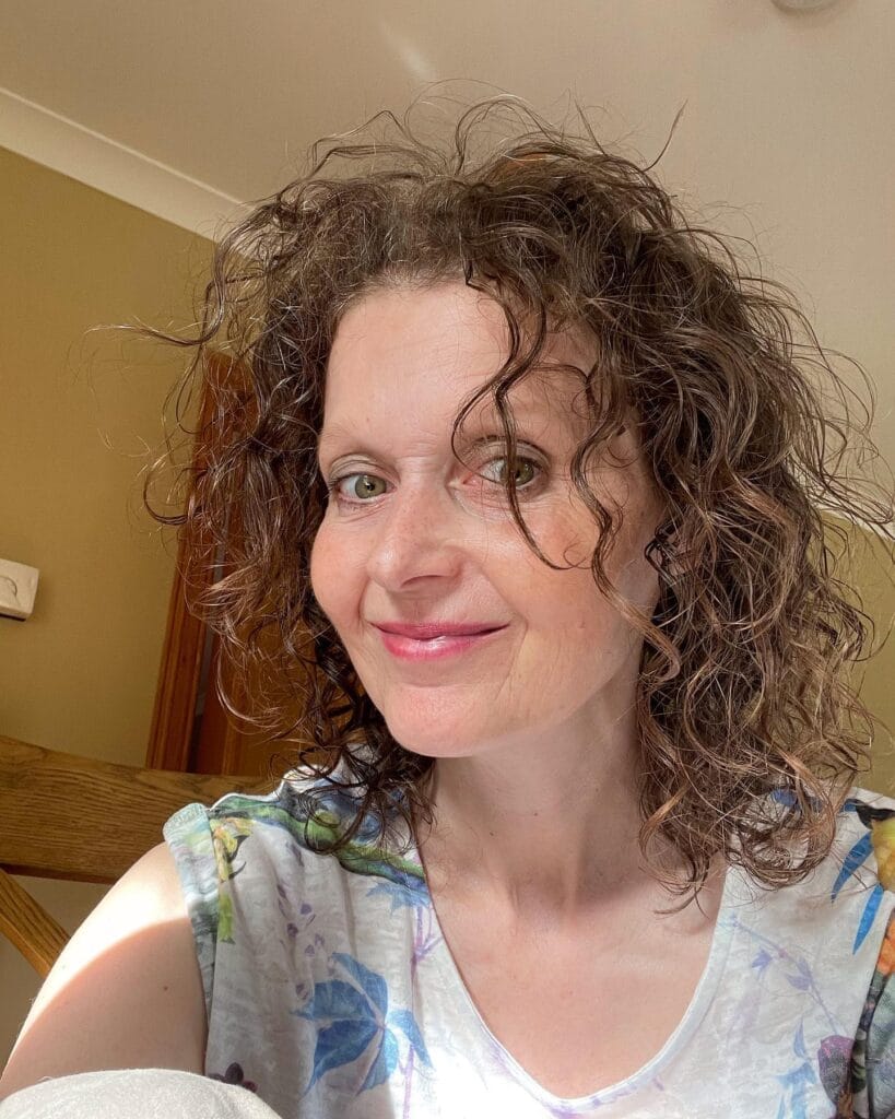 A woman with shoulder-length mahogany brown curly hair smiling for a close-up photo.