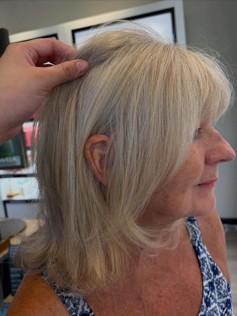 A side profile of a woman with shoulder-length ash blonde hair featuring soft layers and slightly flicked ends.