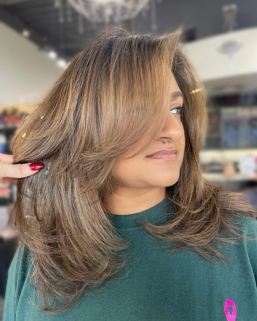 A woman with a voluminous honey brown butterfly cut featuring heavy feathered layers and a bouncy blowout.