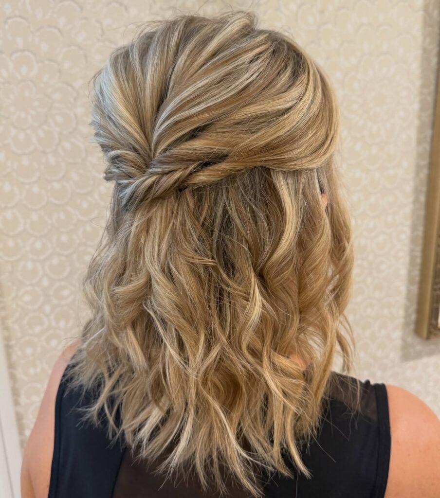 A back view of a woman with mid-length sandy blonde wavy hair styled in a twisted half-updo.