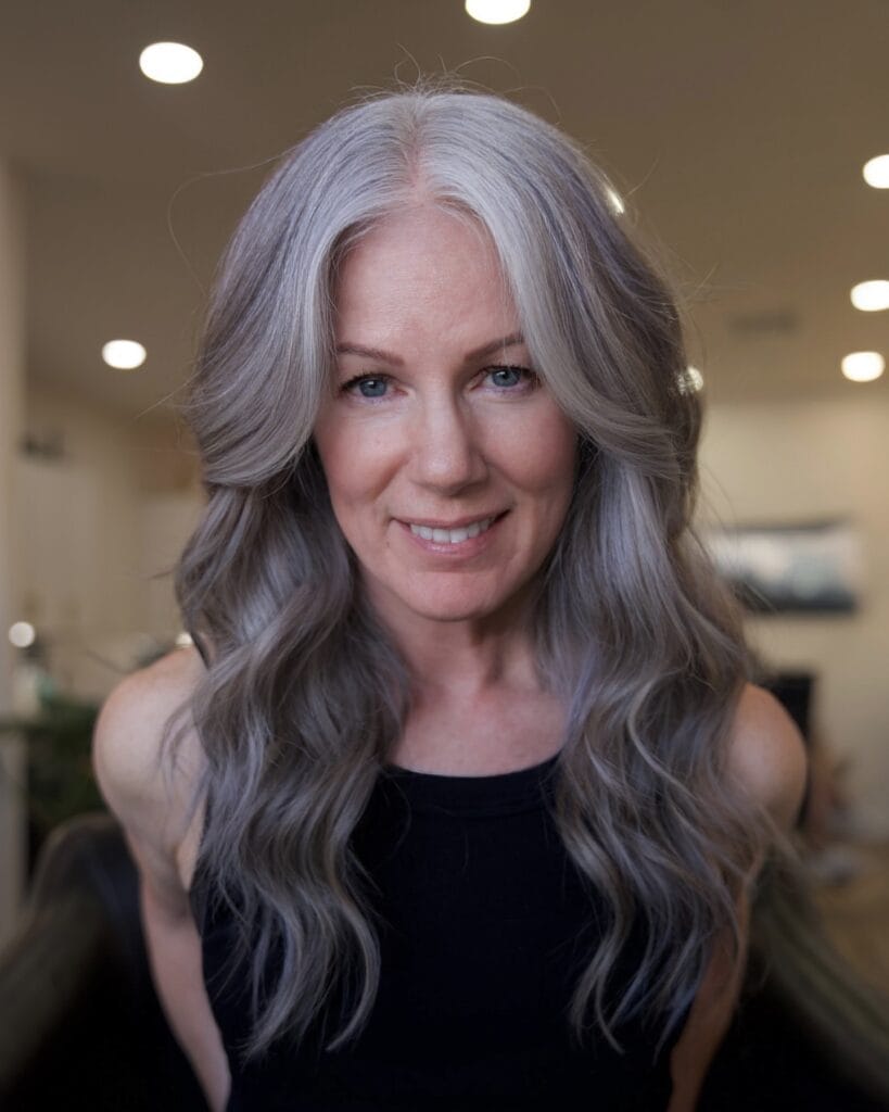 A woman with long, flowing silver hair styled in soft, romantic waves with face-framing layers.