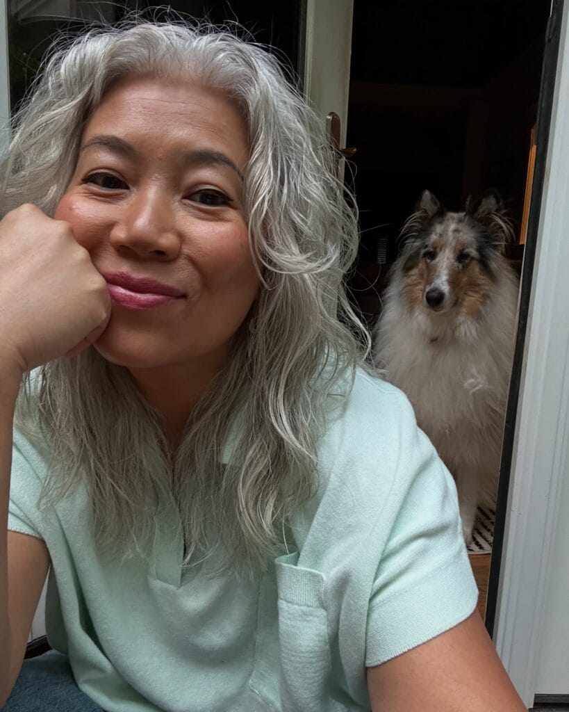 A smiling woman with long, layered, wavy, sterling silver hair and a light green shirt.