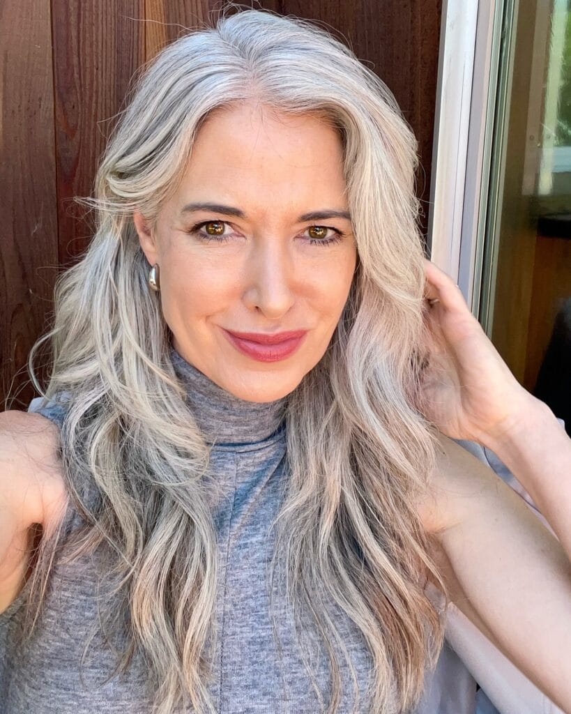 A woman with long platinum silver hair styled in soft cascading waves and face-framing layers.