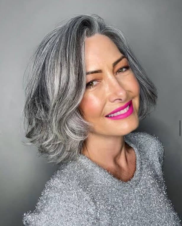 A woman with a chin-length steel silver wavy bob and a deep side part smiling brightly.