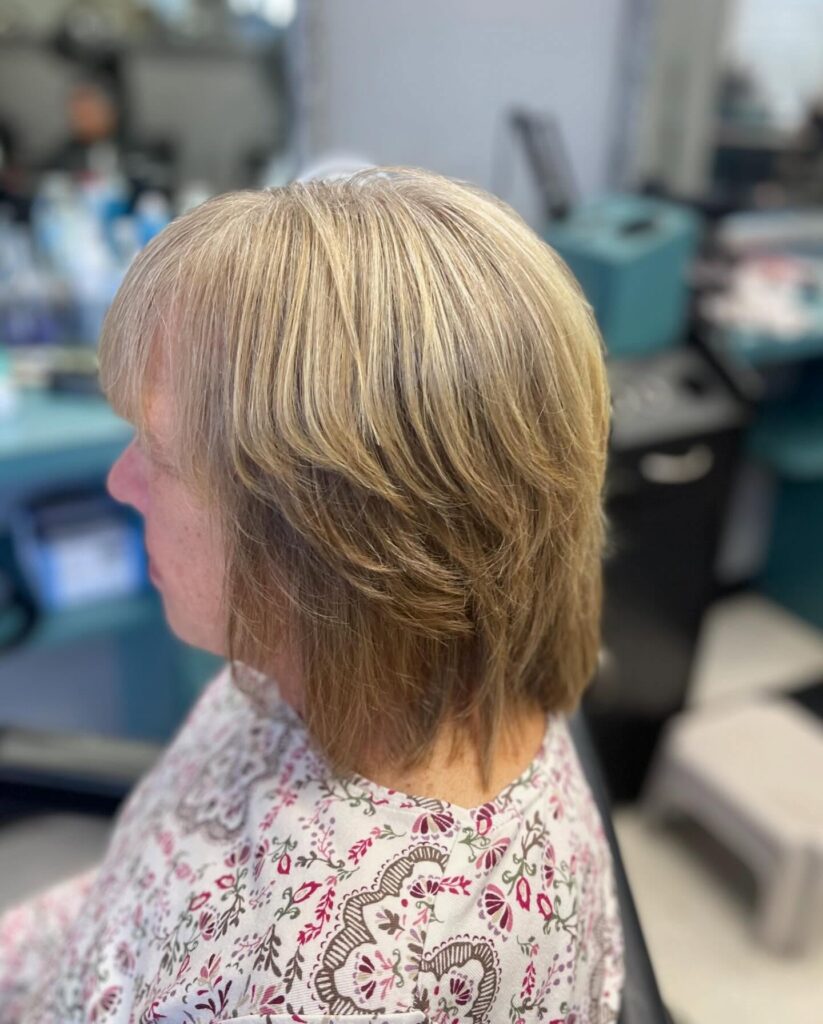 A woman with a medium-length sandy-blonde haircut featuring short feathered layers and soft bangs.