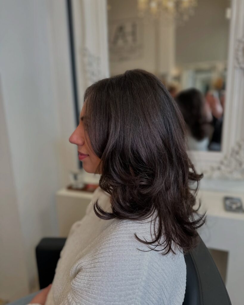 A woman with medium-length dark brown hair featuring voluminous layers and ends that are flipped outward.