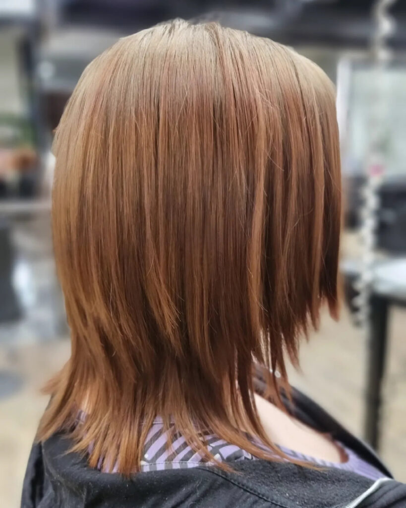 A person from behind showing a medium-length copper haircut with sharp, choppy razor layers and a straight finish.