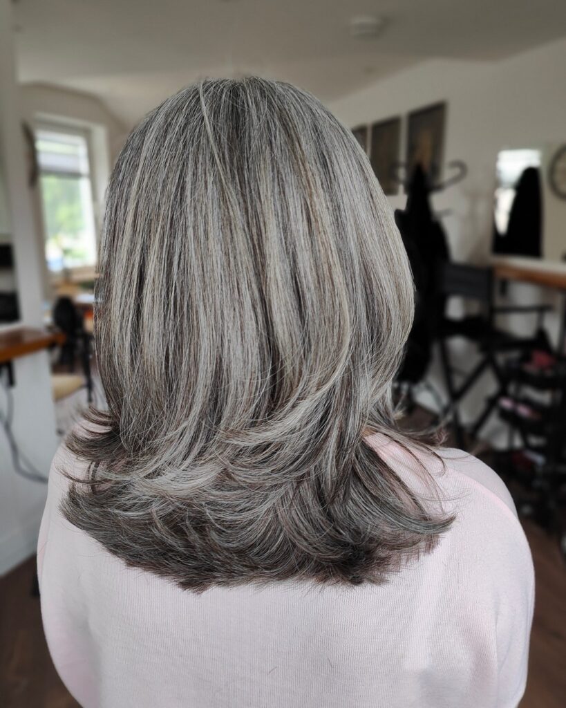 A woman from behind with medium-length silver and gray layered hair featuring ends that are flicked outward.