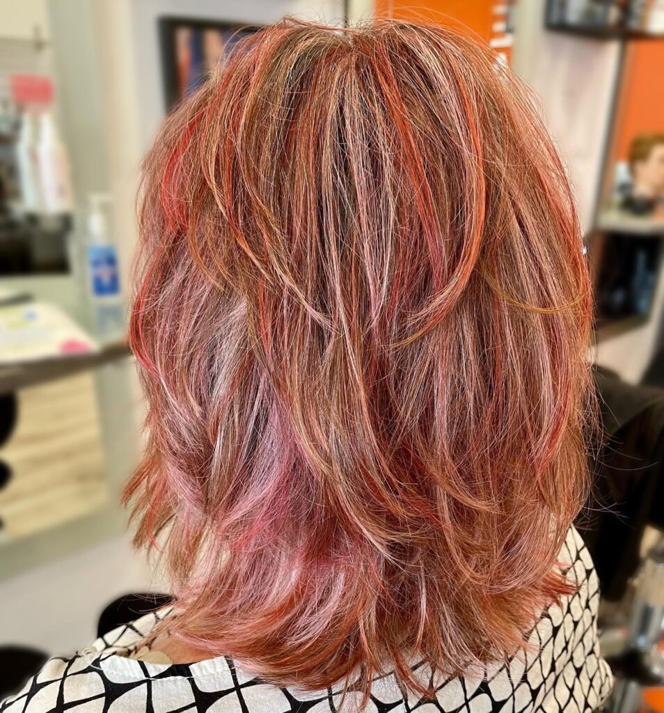A person from behind showing a medium-length haircut with rose and copper highlights and many choppy layers.