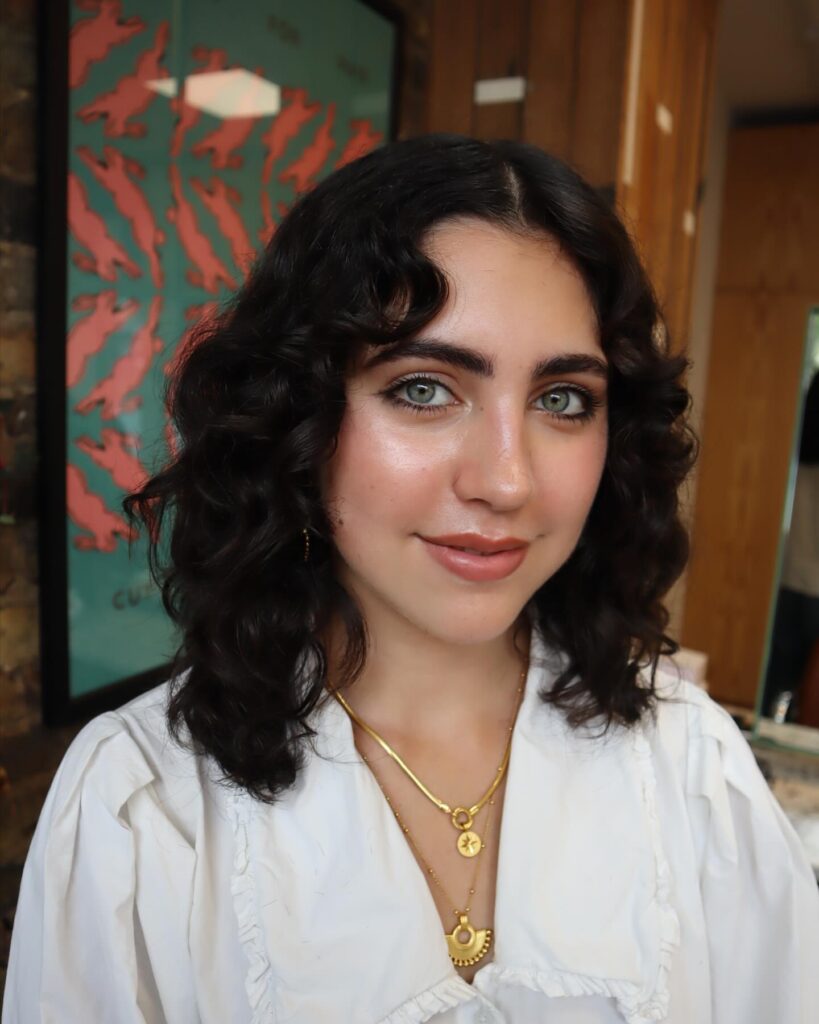 A woman with medium-length dark brown wavy hair styled with a middle part and soft romantic layers.