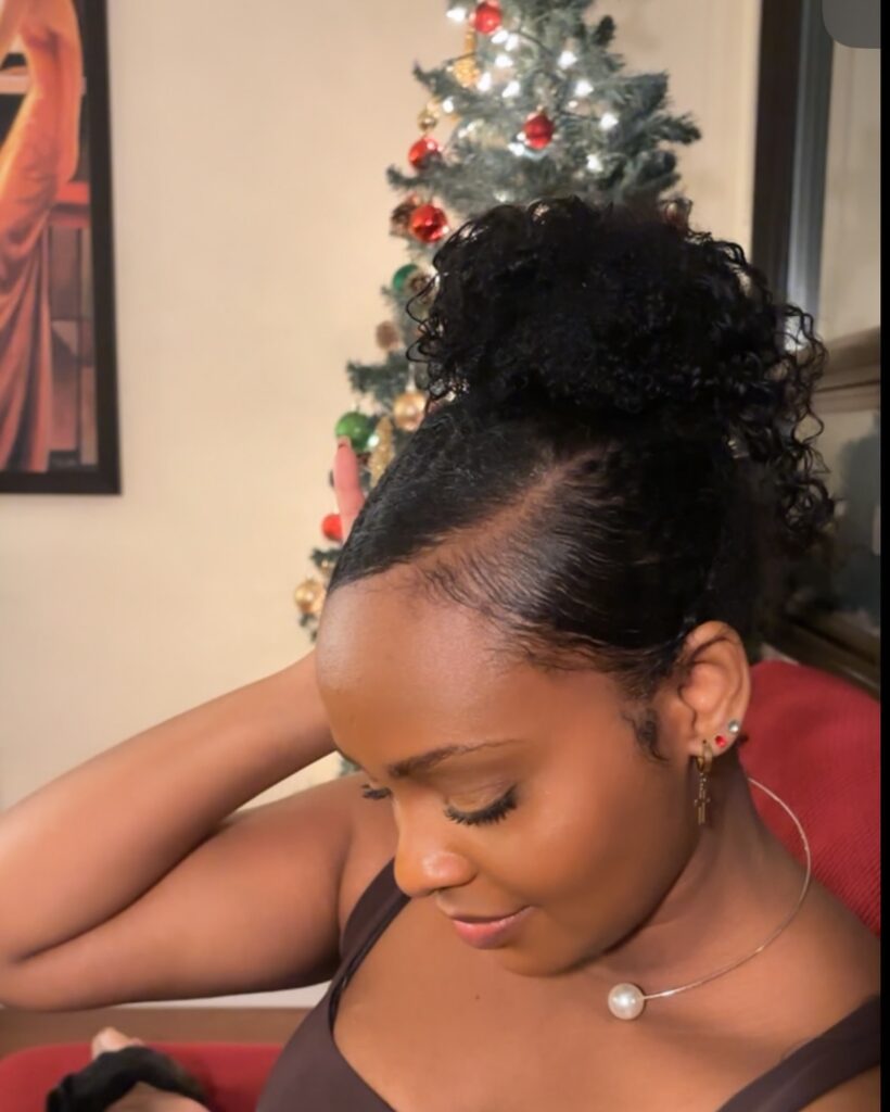 A woman with dark curly hair styled into a high, sleek bun with a clean side part.