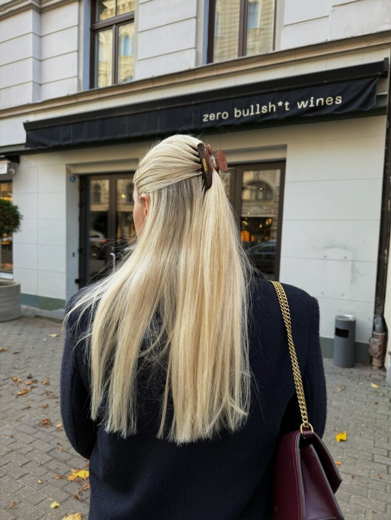 A woman with long straight blonde hair wears a sleek half-up style secured with a tortoiseshell claw clip.