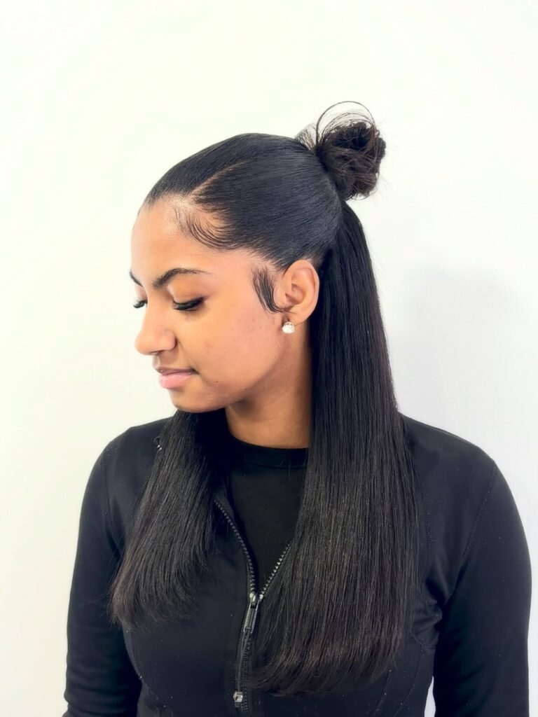 A woman with long, straight black hair wears a sleek half-up style with a small neat bun and styled baby hairs.