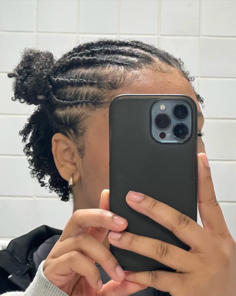 A side view of a woman with short coily hair featuring side braids pulled into a small half-up bun.