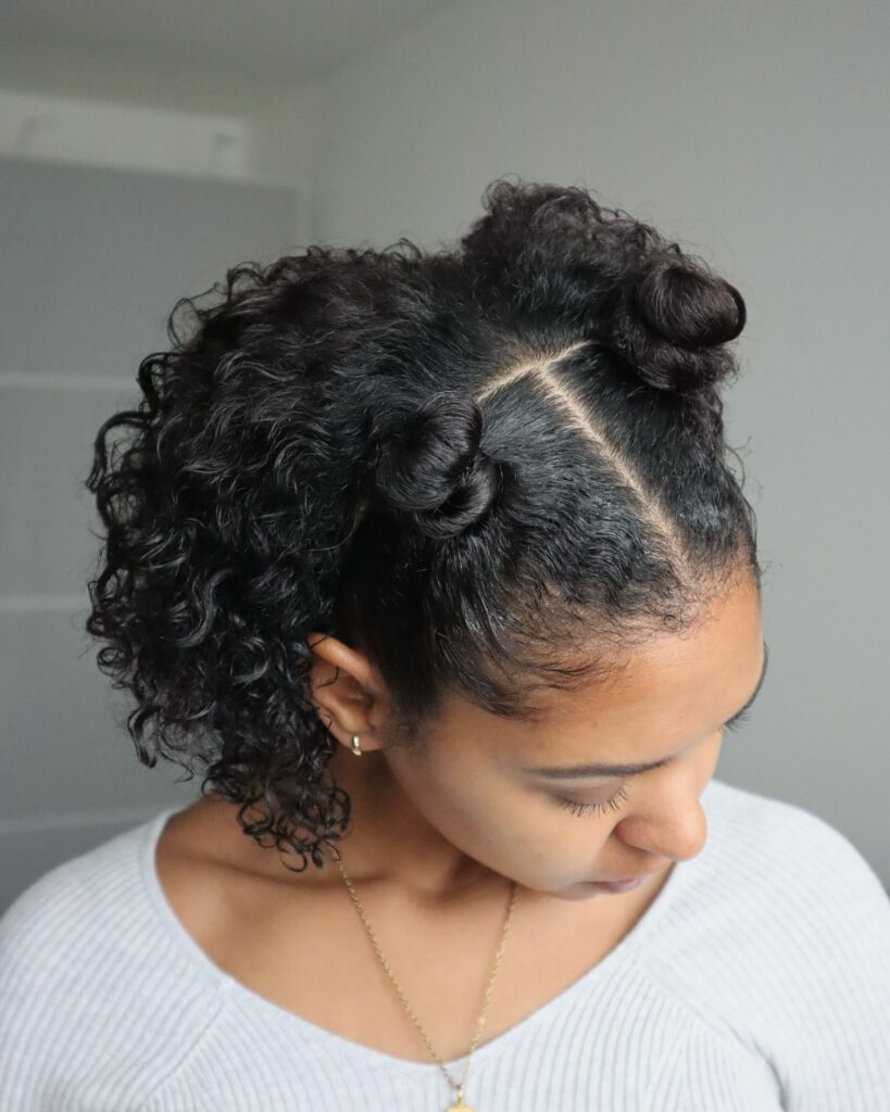 A woman from an overhead angle, showing her dark curly hair styled into two small buns at the top with the rest of her curls flowing down.