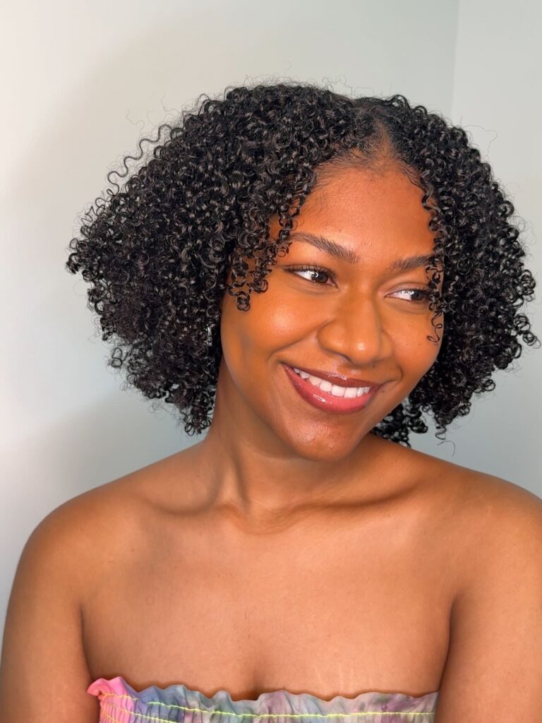 A smiling woman with a short middle-parted bob consisting of very tight black glossy coils.