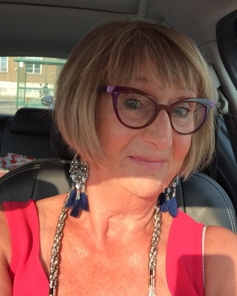 A woman with a chin-length honey blonde pageboy bob featuring soft bangs and inward-curving ends.