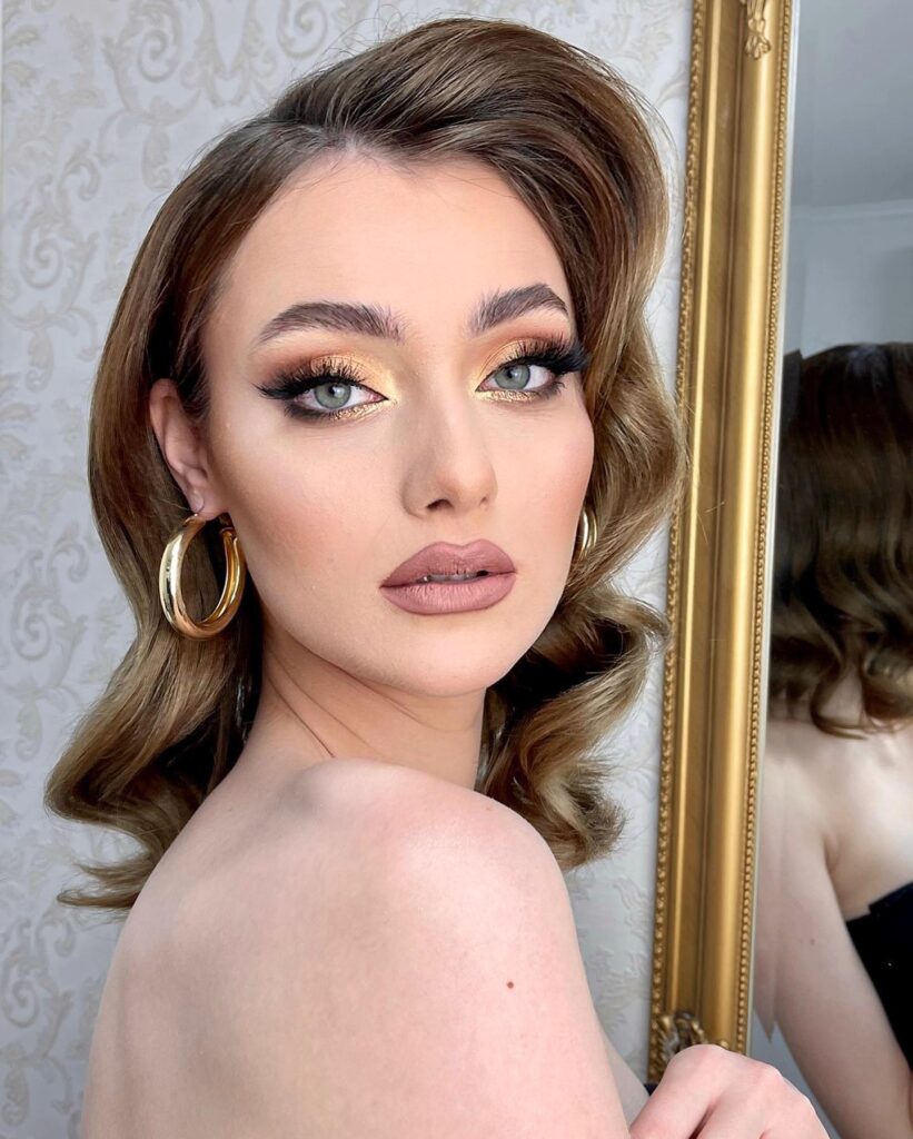 A woman with medium-length caramel brown hair styled in voluminous retro waves with a deep side part and smooth texture.