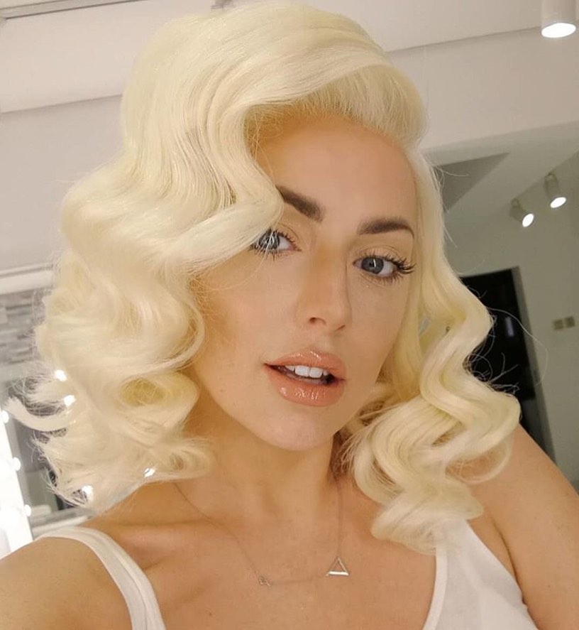 A woman with shoulder-length icy blonde hair styled in voluminous and structured vintage waves with a side part.