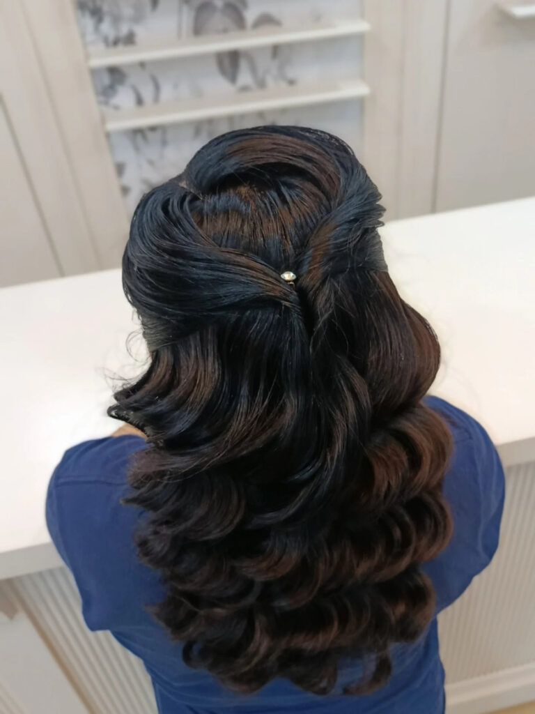 A woman from the back with long dark hair styled in a half-up twisted design with thick vintage waves.