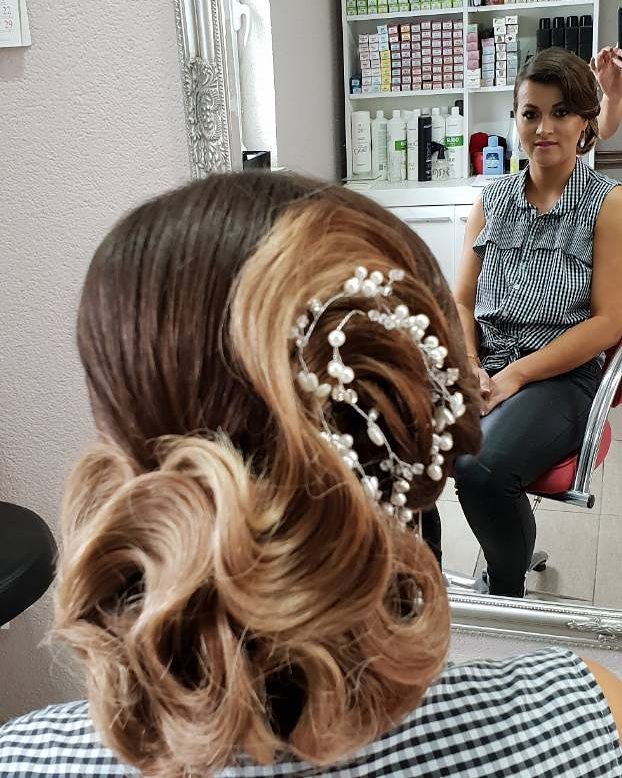 A woman from the back with brunette and honey blonde hair styled in an intricate retro updo with a decorative pearl hair vine.