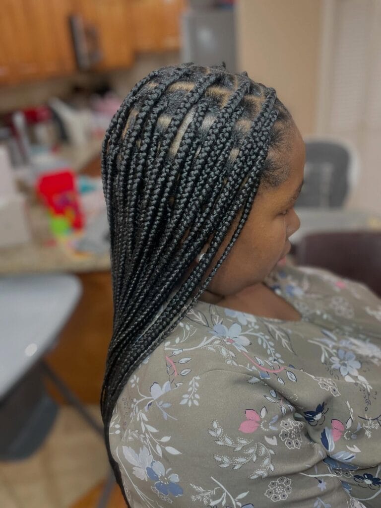 A person shows off neat jet black feed in straight back cornrows with clean parting lines.