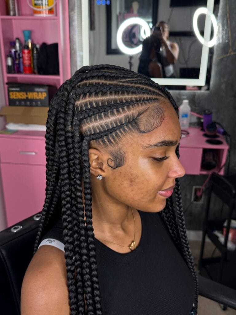A woman shows off thick jet black stitch cornrows with intricate curved baby hair designs along the hairline.