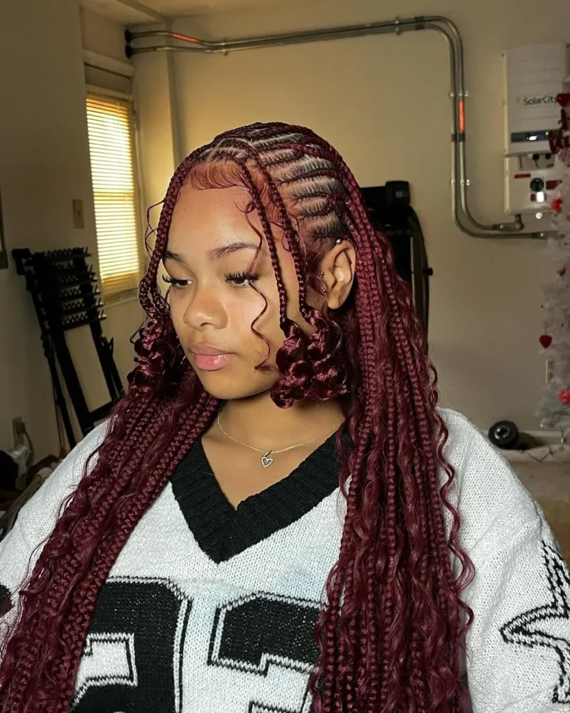 A woman showcases long burgundy cornrow braids that transition into voluminous wavy ends with decorative face framing curled tendrils.