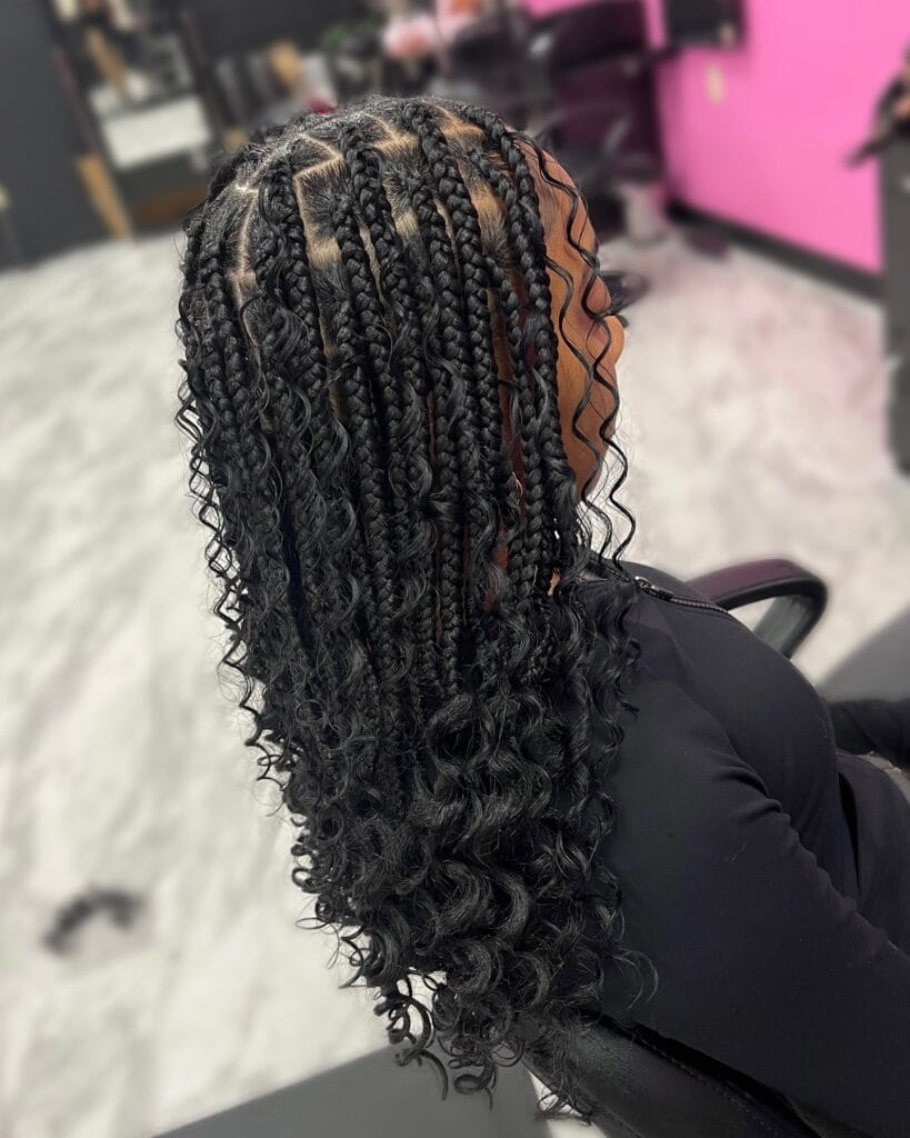 A back view of a person with mid length black goddess braids featuring bouncy curls mixed with sleek braids.