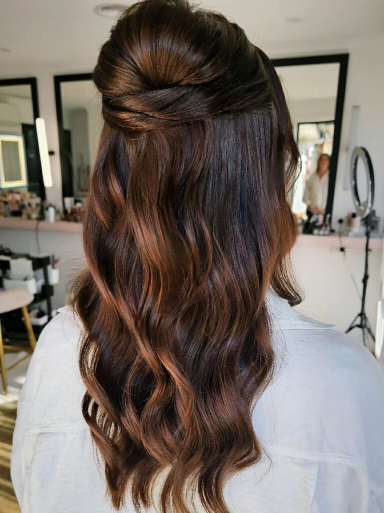 A woman with long wavy chestnut brown hair styled in a voluminous half up look with overlapping horizontal twists.
