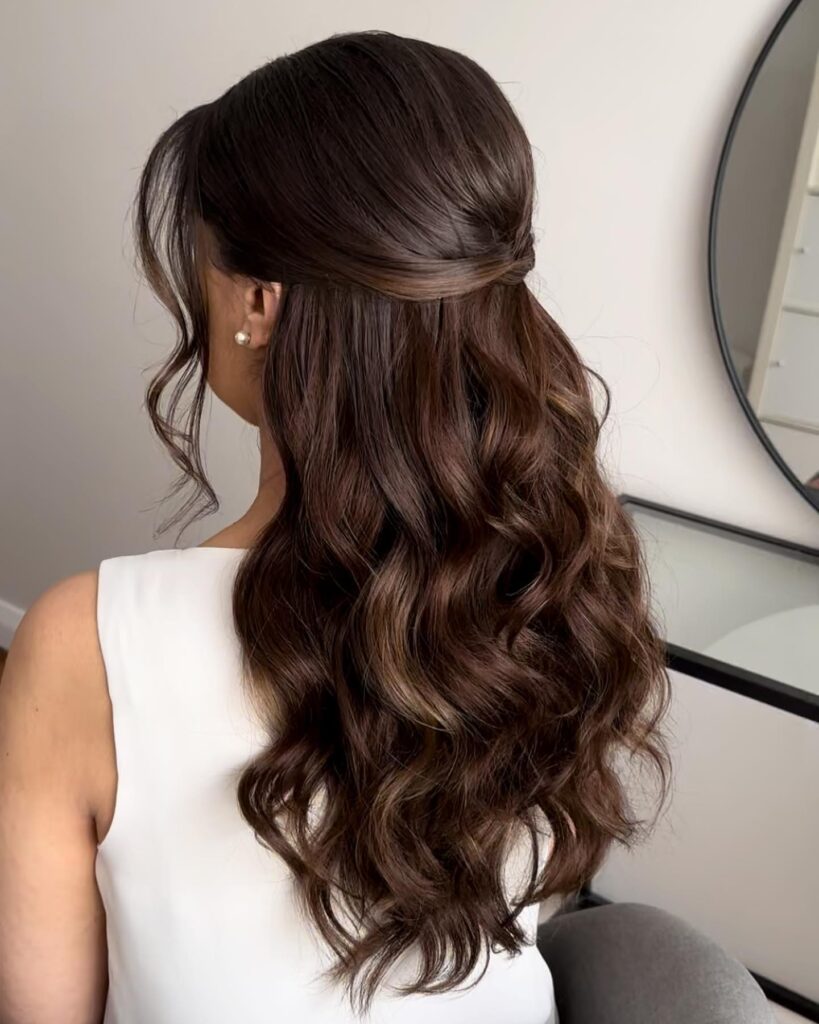 A woman with long wavy dark brown hair in a half up twisted knot hairstyle seen from behind.