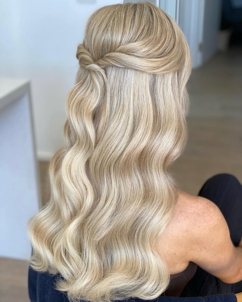 A woman with long wavy blonde hair styled in a half up half down look with a twisted topsy tail in the back.