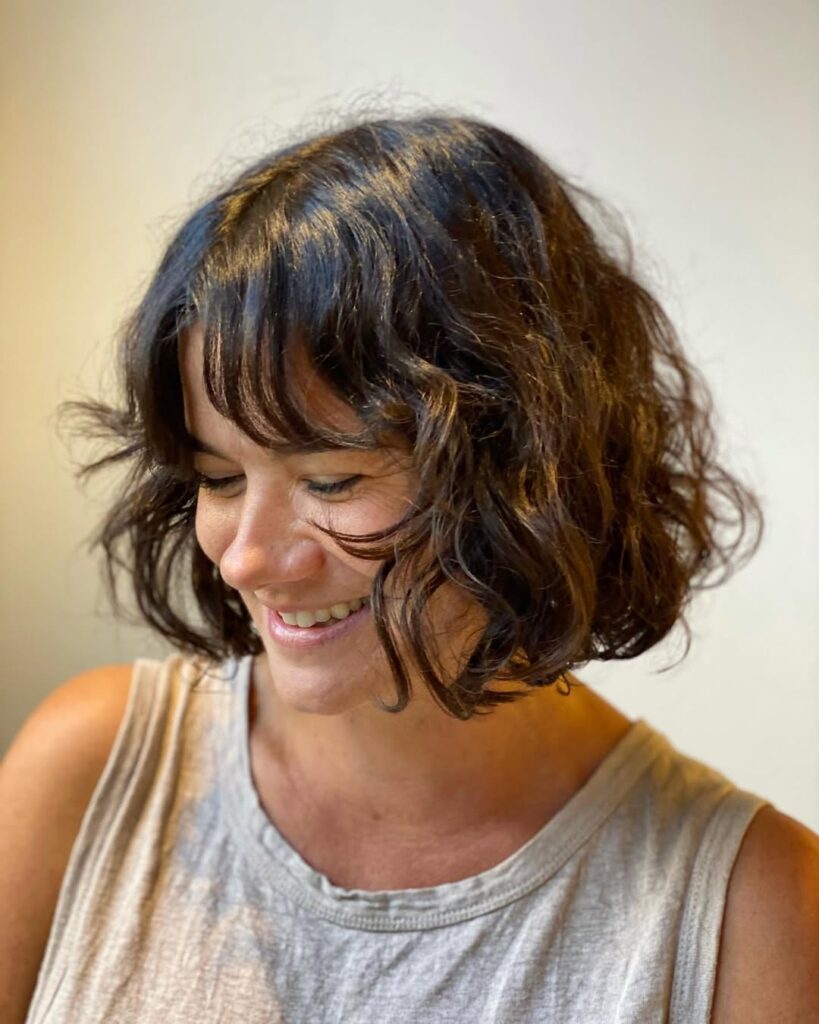A woman with a wavy long bob and soft curtain bangs in a medium brown tone.